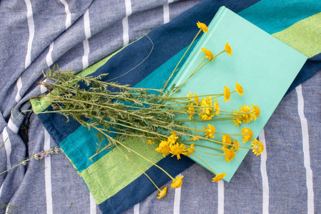 Book and yellow flowers on a fabric background outdoors. Relaxing in nature, summer vacation, enjoying reading a novel.の写真素材