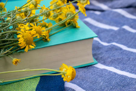 Book and yellow flowers on a fabric background outdoors. Relaxing in nature, summer vacation, enjoying reading a novel. Top viewの写真素材
