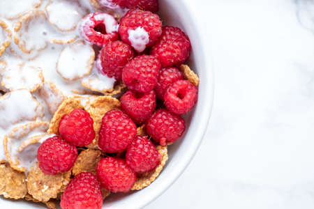 Bowl of multigrain cereal with yogurt and fresh raspberry berries on marble table background. Healthy diet breakfast. Top view, flat lay, copy spaceの写真素材