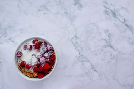 Bowl of multigrain cereal with yogurt and fresh raspberry berries on marble table background. Healthy diet breakfast. Top view, flat lay, copy spaceの写真素材