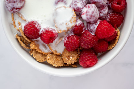 Bowl of multigrain cereal with yogurt and fresh raspberry berries on marble table background....