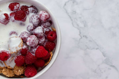 Bowl of multigrain cereal with yogurt and fresh raspberry berries on marble table background. Healthy diet breakfast. Top view, flat lay, copy spaceの写真素材