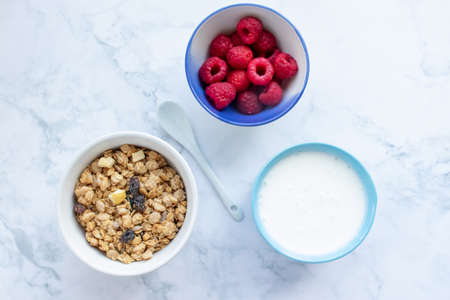 Bowl of homemade granola cereal with greek yogurt and fresh raspberry berries on white marble table background. Top view, flat lay, copy space. Healthy eating concept.の写真素材