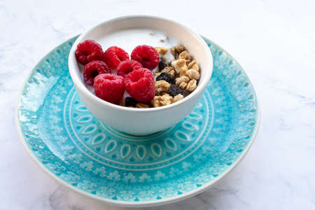 Bowl of homemade granola cereal with greek yogurt and fresh raspberry berries on white marble table background. Top view, flat lay, copy space. Healthy eating concept.の写真素材