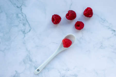 Raspberries in a white plastic spoon on a marble background.の写真素材
