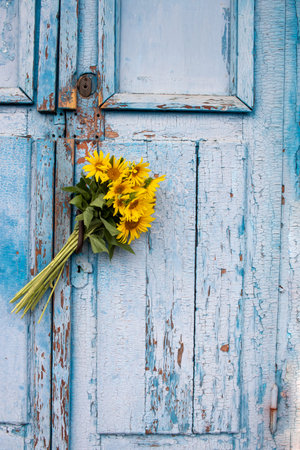 Bouquet of sunflowers on a blue wooden background. Old blue wooden door with yellow flowers. Copy spaceの写真素材