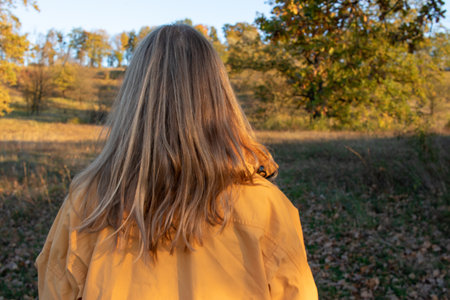 Portrait of a woman with long blonde hair in autumn park. Back viewの写真素材