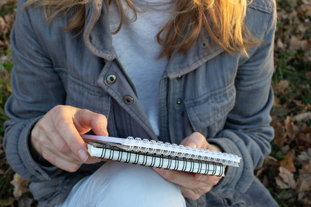 Woman in holding sketchbook and a pencil outdoors. Close-up of hands with notebook and pencil....