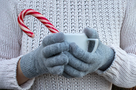 Hand holding a cup of tea, coffee, cocoa or hot chocolate. Woman in white knitted sweater and gray gloves holding cup of hot drink. Close upの写真素材