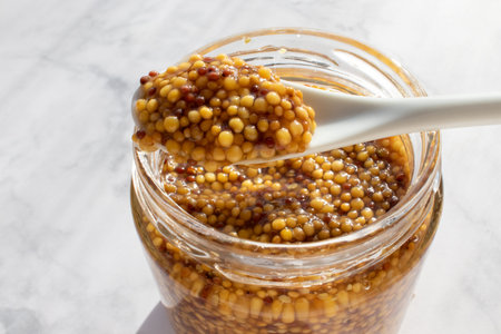 Mustard in a glass jar with a spoon on a marble background