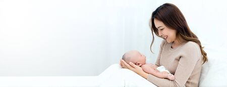Beautiful mom cuddles the newborn baby gently while the infant is sleeping on the lap. Asian mother looking at the baby with love and showing protection.の写真素材