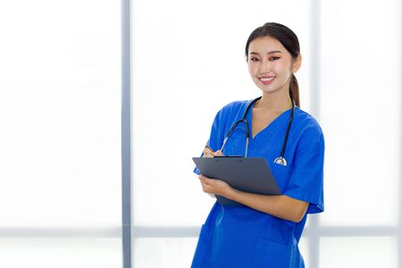 Portrait of attractive Asian medical staff is standing and smiling while holding a clipboard in her hands.の写真素材