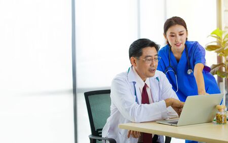 Asian surgery doctors is meeting the treatment plan into office. Physicians in uniform dress working with laptop on the desk in which colleagues talking about the surgical procedures for patients.の写真素材