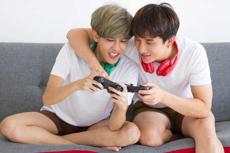 Happy Asian homosexual men or gay couples are playing video games on the sofa together. Concept of LGBTQ pride.の写真素材