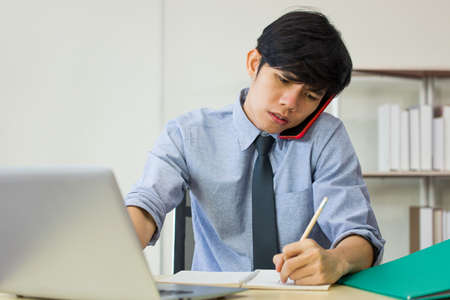 Employee man is busy with work on the desk. The male worker was talking on the phone while his hand was writing the order from the customer.の写真素材