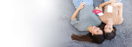 Two young Asian women lying on the floor and holding passports smiling happily. Pretty girls planning a vacation trip in the summer at home.の写真素材
