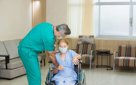 A Nursing man is pushing an old woman's wheelchair in a hospital corridor to take relax while recovering from illness.の写真素材