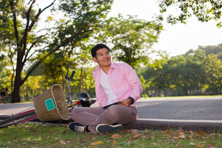 Asian man sitting relaxed in the park with bicycle and tablet.の写真素材