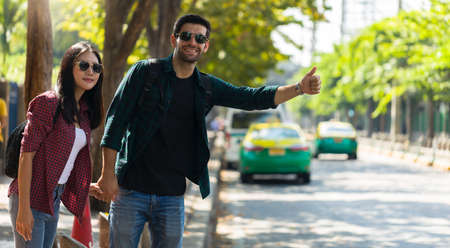 Couple travelers are holding hands together waiting for taxi car in the city street.の写真素材