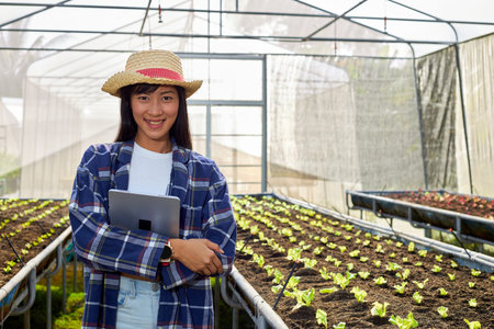 Young female farmer holds a tablet in a greenhouse filled with organic vegetables.の写真素材