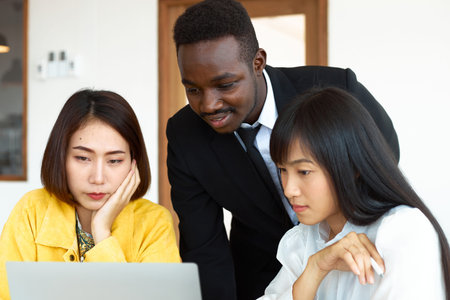 A black male waiter introducing a menu to a young Asian woman inside the restaurant, all looking at the front paper.の写真素材