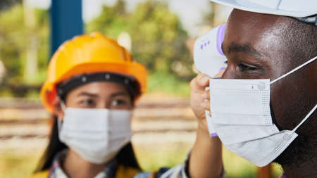 Industrial workers who are screened for disease before entering an industrial plant. Measures to prevent pandemic  within the factory. Labor was taking a forehead temperature measurementの写真素材