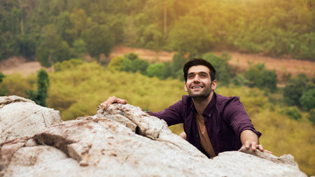 A handsome caucasian man is trying to climb a rock to the top of the mountain during vacation trips. Concept of trying to focus on goals and success.の写真素材