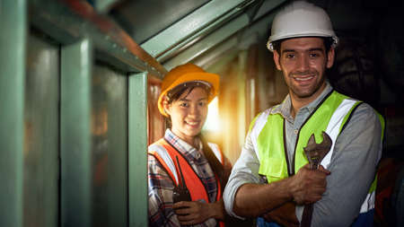 Machine engineers or factory mechanical technicians and assistants wearing helmets and safety suits are standing with a wrench and looking at the camera in the industrial machinery room.の写真素材