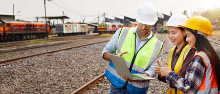 Successful Rail logistics specialists or train engineers wearing helmets and safety vests are conducting inspections and meeting a work plan for managing a freight train on the train tracks.の写真素材