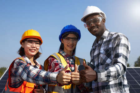 A group of ethnically diverse electrical engineers wearing helmets and safety vests were thumbs up to show unity in the outdoors. Solar Power Management and Alternative Energy, Clean Energy.の写真素材