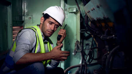 A mechanical engineer or a machine maintenance technician in protective clothing is chatting with a walkie-talkie while checking the machine's readiness in the workshop within the factory.の写真素材