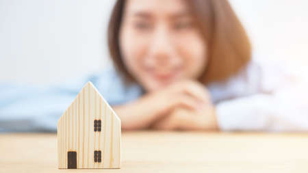 Blurred of a woman looking at a replica wooden home happily and dreams of owning a house. Residential buying ideas and real estate loan applications.の写真素材