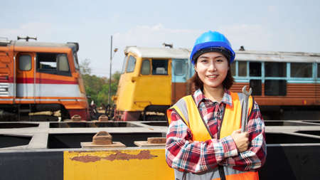 A female maintenance technician in a safety suit stands beside a freight train with the wrench. Asian woman workers work within the rail transport industry.の写真素材