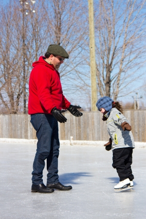 Father teaching daughter how to ice skate at an outdoor skating rink in winter の写真素材