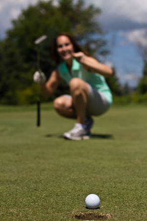 Woman sinking a putt on a golf greenの写真素材
