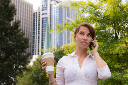 Woman with coffee in the urban park using smart phoneの写真素材