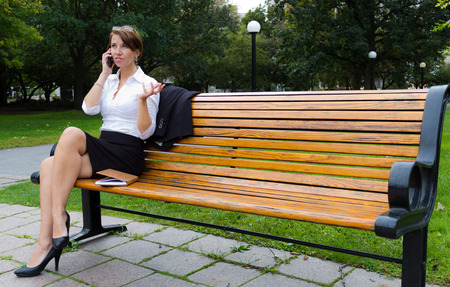 Business woman in the park talks on mobile phoneの写真素材