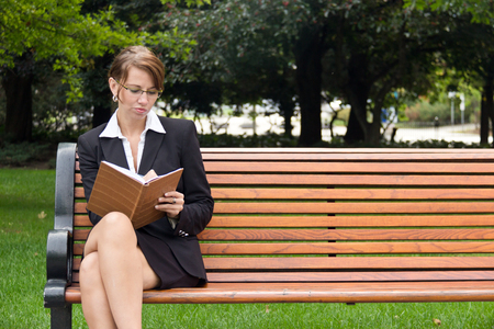 Stylish business woman siting on park bench writing in notebookの写真素材