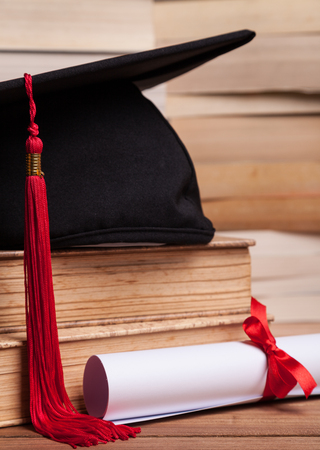 Mortarboard with red tassel, diploma, and books on a tableの写真素材