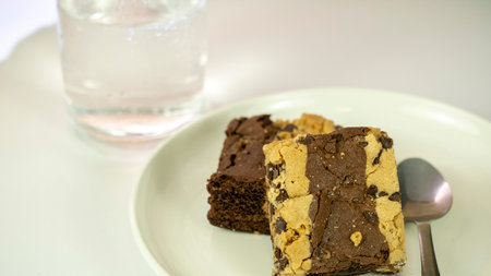 Brownies on a white plate with a glass of water in the backgroundの写真素材
