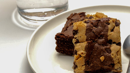Chocolate brownies on a white plate with a glass of waterの写真素材