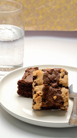 Chocolate brownies on a white plate with a glass of waterの写真素材