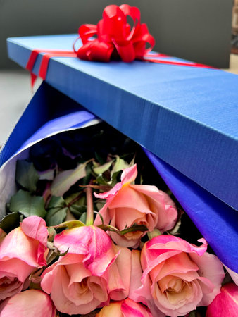 Bouquet of pink roses in a blue gift box with a red ribbonの写真素材