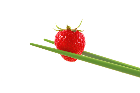 red strawberry hold with green chopsticks in closeup white backgroundの写真素材
