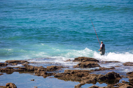A lone fisherman wading into the ocean off the coast of Rabat beachの写真素材