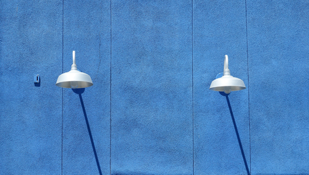 Blue stucco wall with light fixtures and shadows in daytimeの写真素材