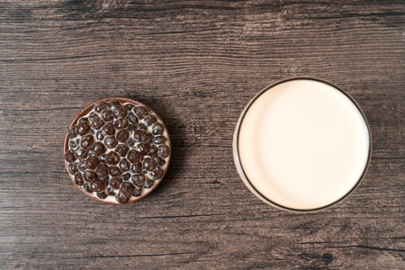 A glass cup of pearl milk tea (also called bubble tea) and a plate of tapioca ball on wooden background. Pearl milk tea is the most representative drink in Taiwan.の写真素材