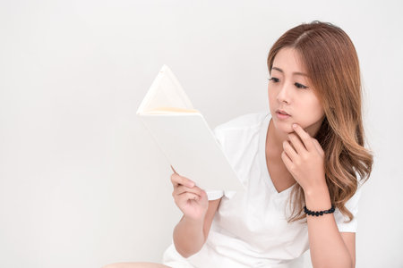 Young attractive asian student holding books in her arm on white background. School girl with a...