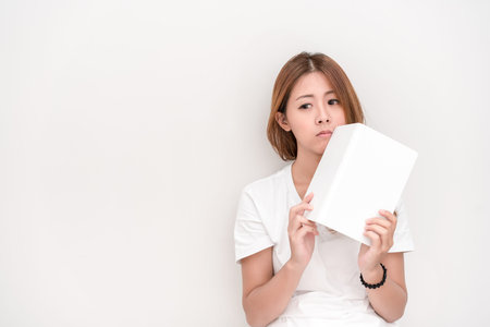 Young attractive asian student holding books in her arm on white background. School girl with a...