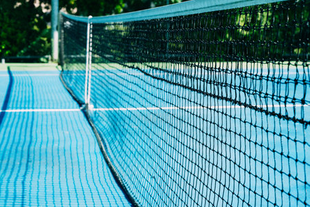 Deserted tennis court with greentrees in background in a public park on a sunny summer morning